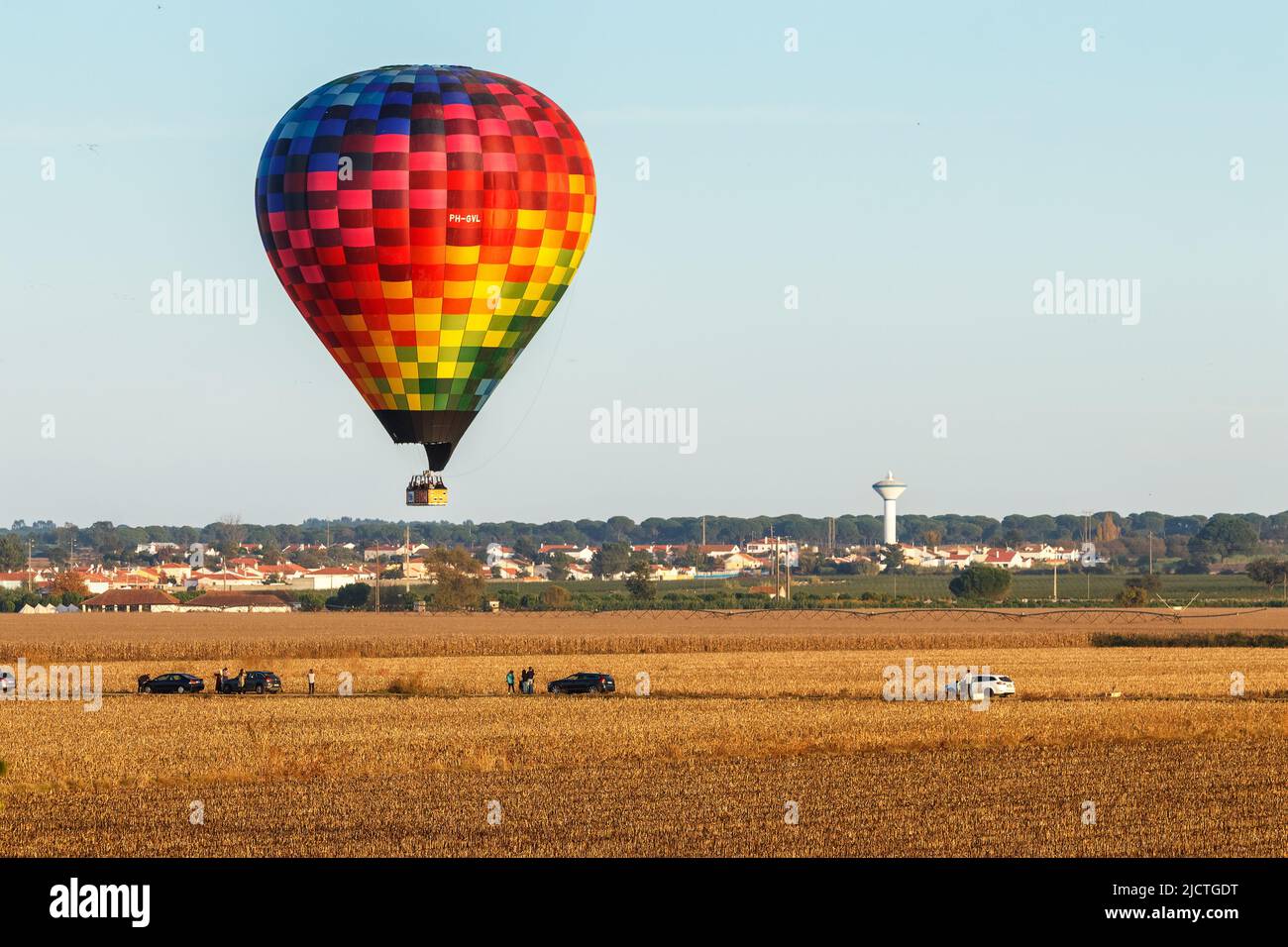 Coruche, Portugal - November 13, 2021: Large hot air balloon flying over cornfields with people watching on a road, near Coruche in Portugal, during t Stock Photo