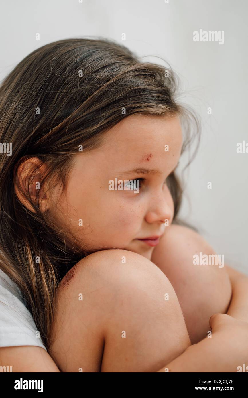 portrait of little sad shocked wounded girl sitting, hugging knees. Protest against domestic violence. Stock Photo