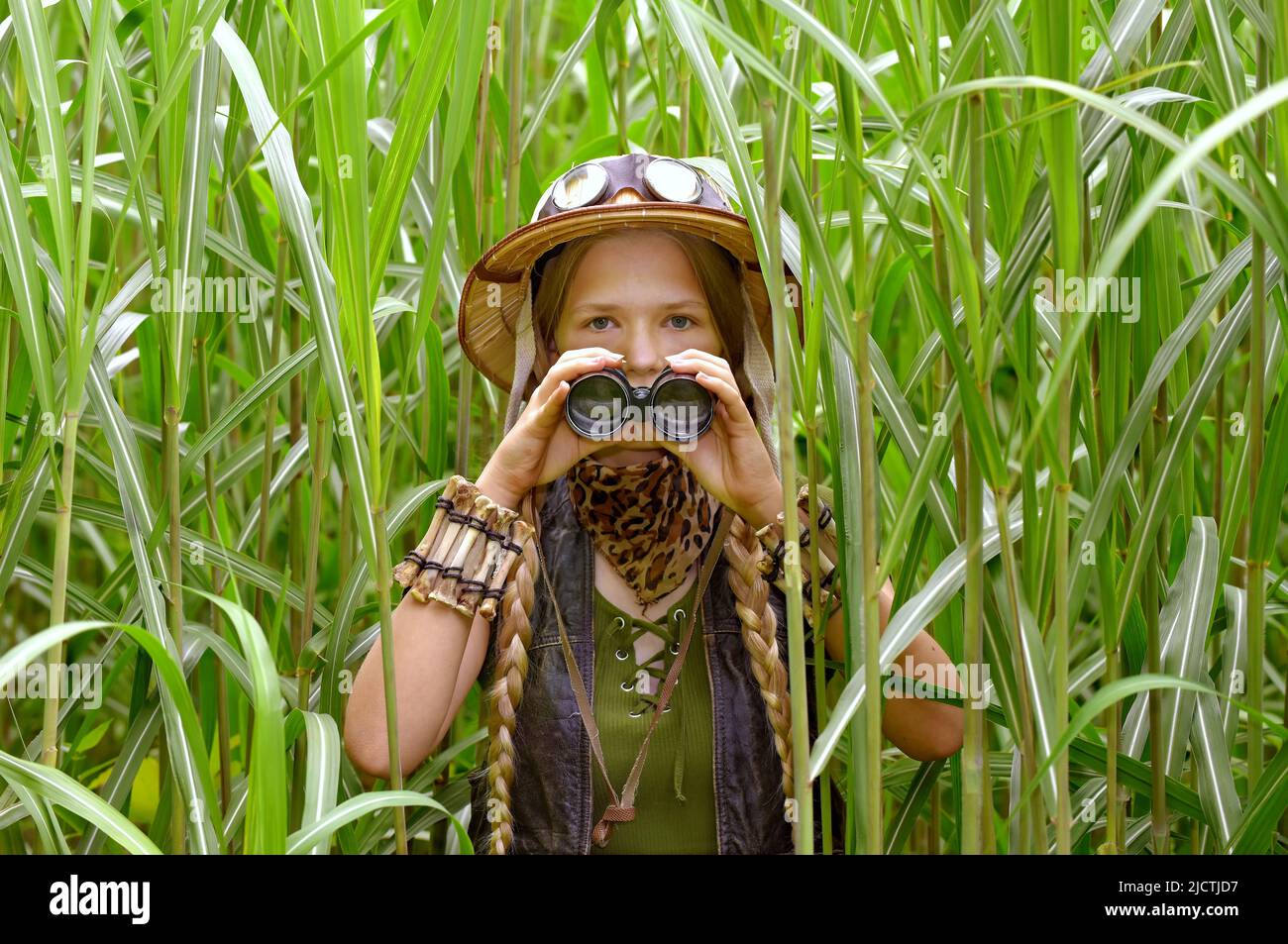 A young teenage explorer is seen in tall grass. She holds a pair of binoculars whilst observing the jungle area. Stock Photo