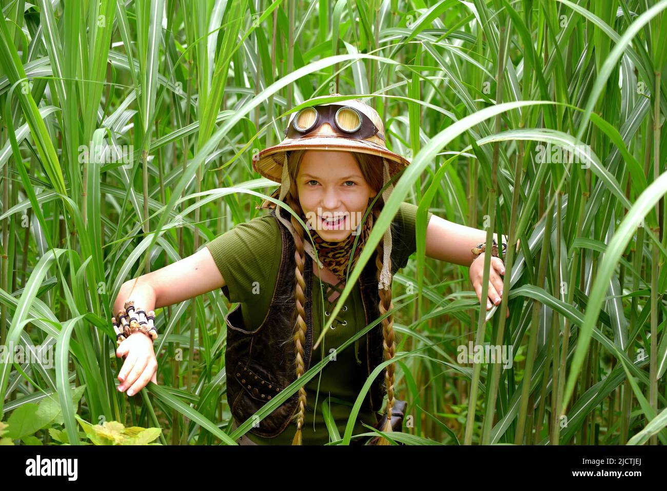 A young teenage explorer is seen in tall grass. She holds a pair of binoculars whilst observing the jungle area. Stock Photo