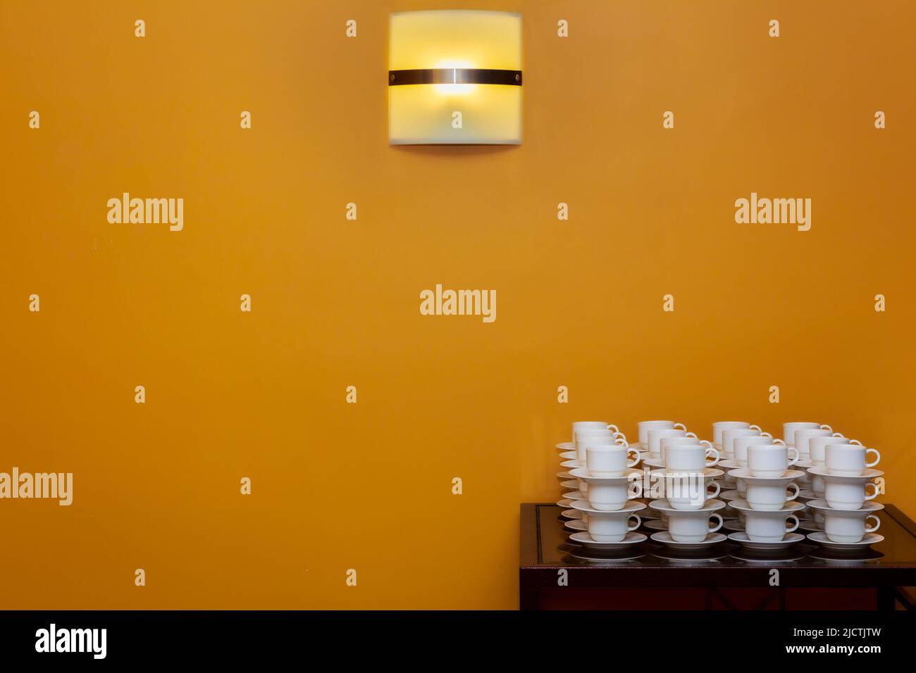 A stack of coffee cups and saucers against an orange feature wall with
