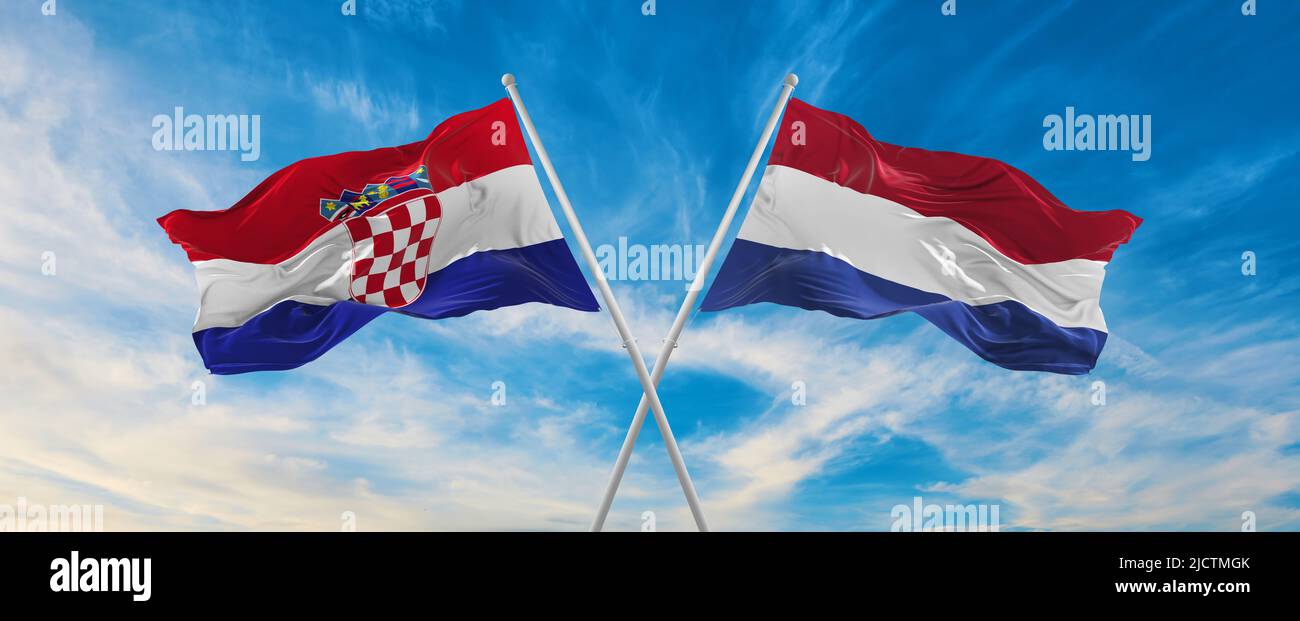 two crossed flags Croatia and Netherland waving in wind at cloudy sky ...