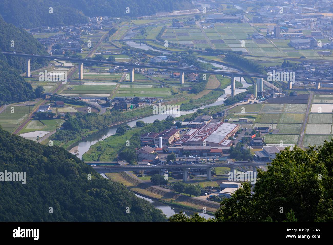 Elevated roadway over winding river and rural rice fields in morning mist Stock Photo