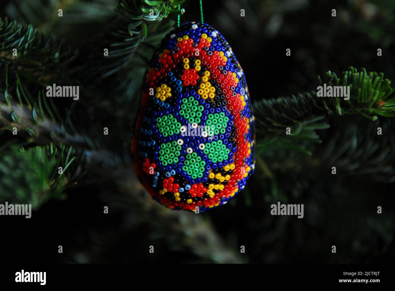 Christmas- Close up of a colorful homemade tree ornament made of egg shaped wax with a pattern of tiny multi colored beads pressed in. Stock Photo