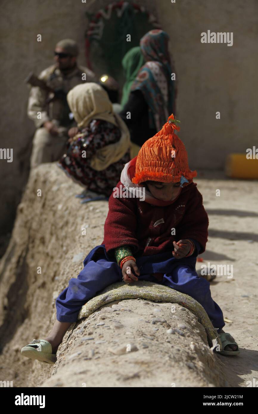 An Afghan child sits and plays while Afghan Task Force (ATF) soldiers question the compound's owner about Taliban activity in Kajaki, Helmond province Stock Photo