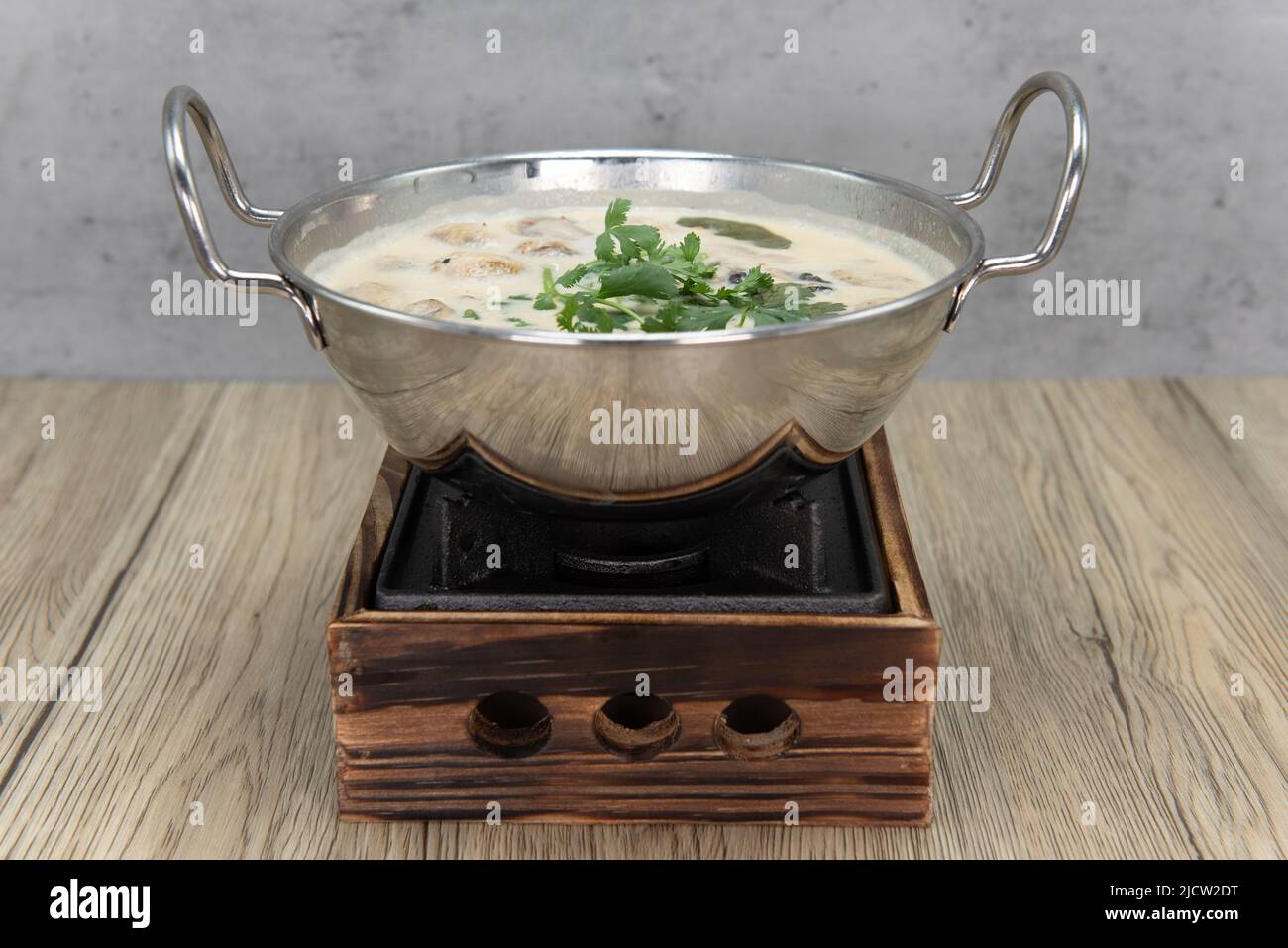 Shiny bowl of Tom Kha Kai presented in a fabulous reflective bowl on a decorative pot. Stock Photo
