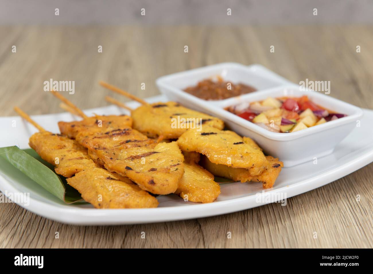 Tangy satay chicken on sticks, served with salsa, dipping sauce and ready to eat. Stock Photo