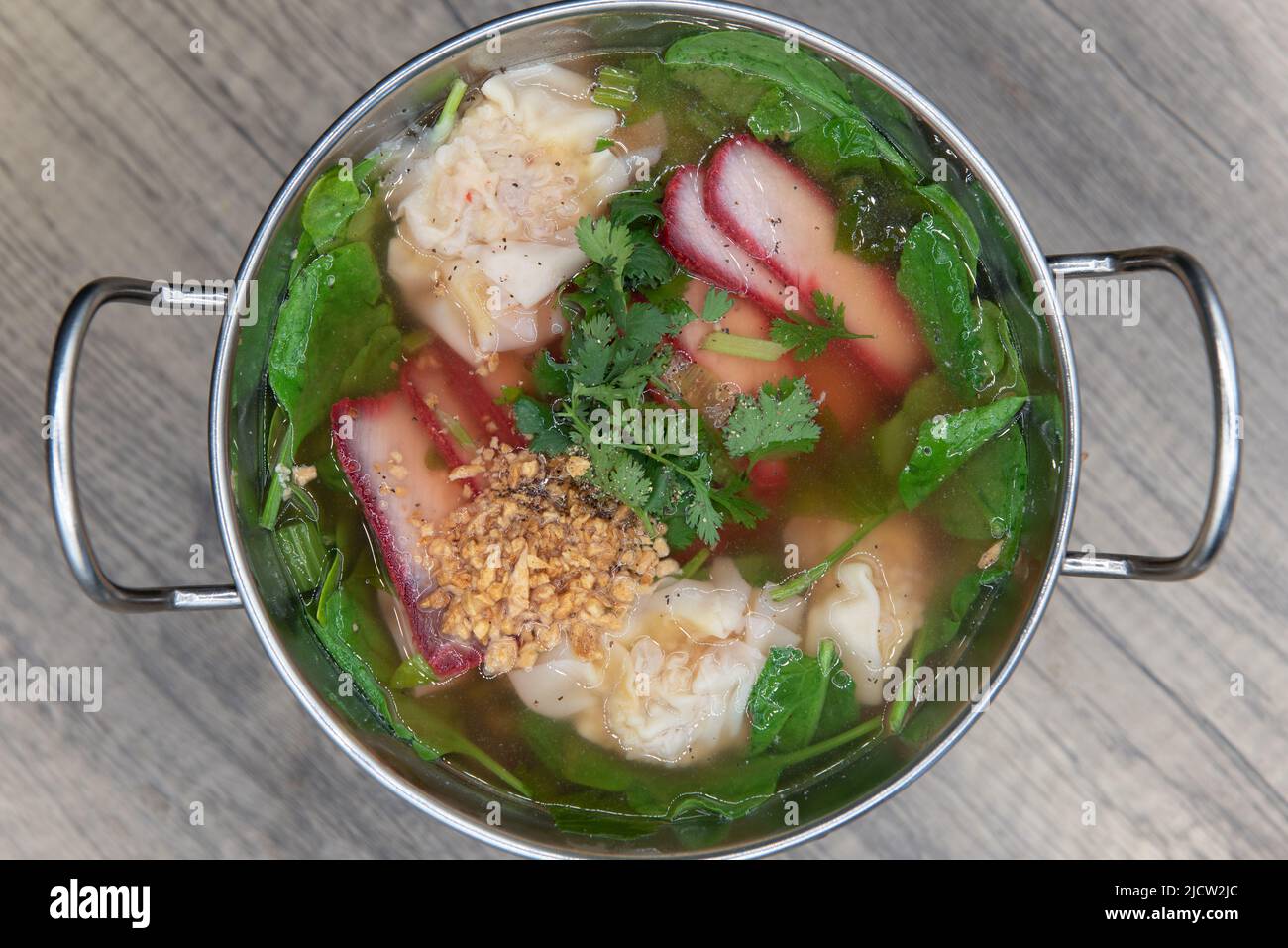 Overhead view of magnificent shiny bowl of wonton soup steaming and ready to eat on table top pot. Stock Photo