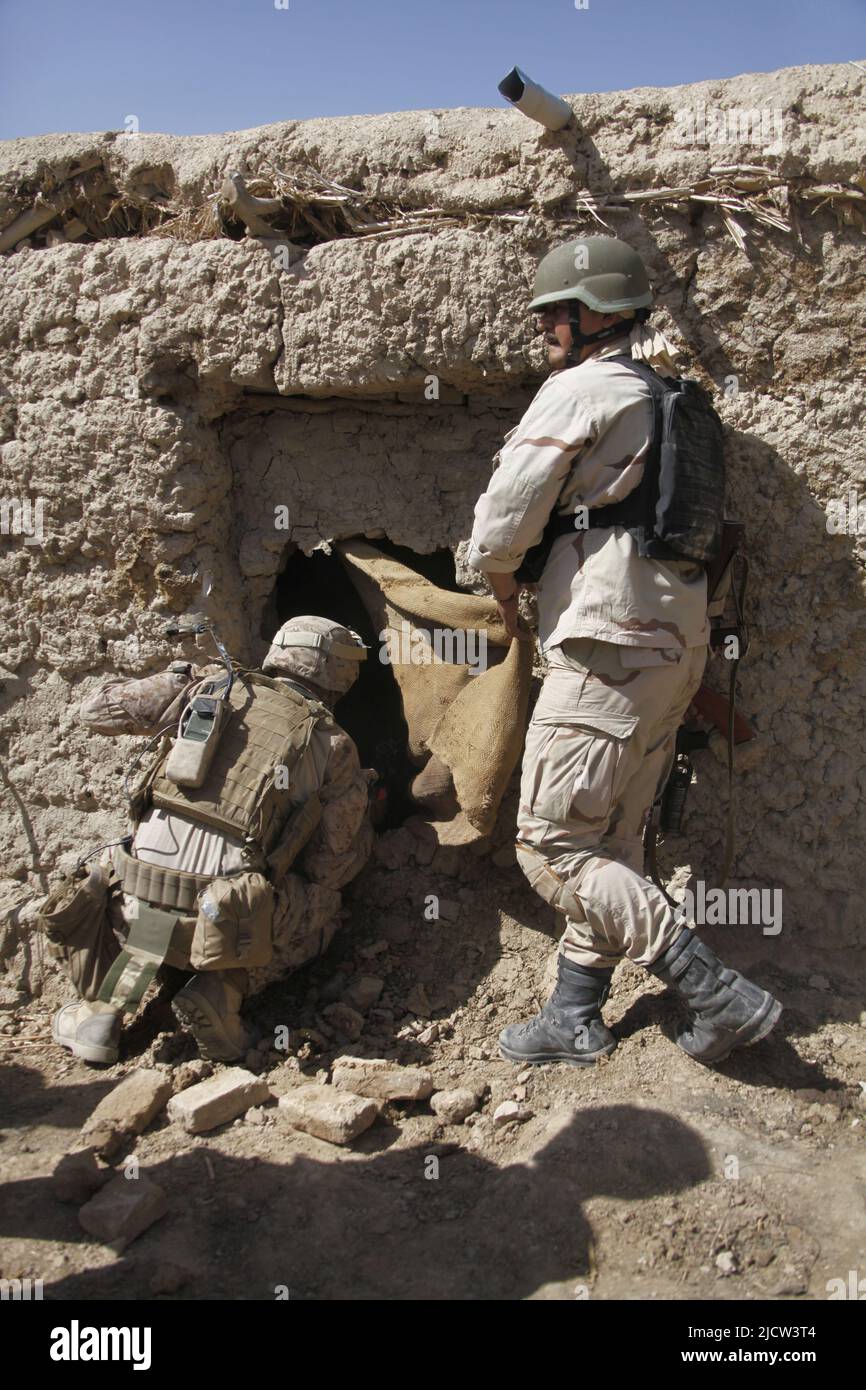 A U.S. Marine (left) with 1st Battalion, 8th Marine Regiment, Regimental Combat Team 6 looks through a hole that was covered up by a curtain with a so Stock Photo