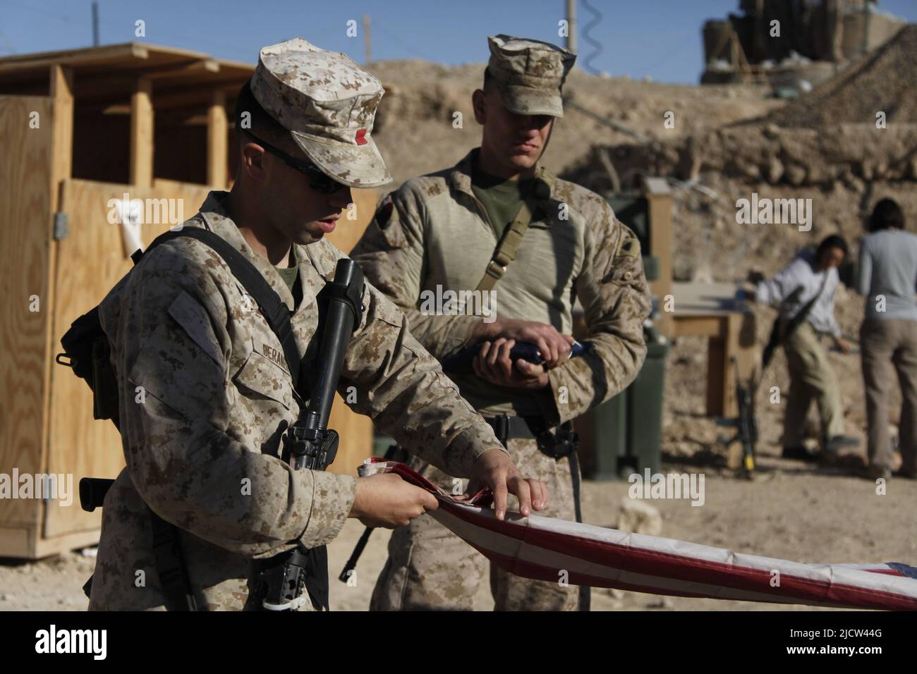 U.S. Marine Corps Sgt. James M. Mercure Jr. (right) with 1st Marine Expeditionary Force Forward, holds a folded American flag that is going to be rais Stock Photo
