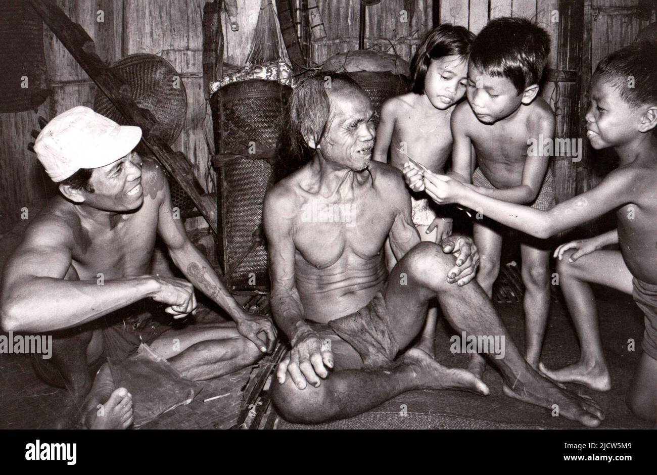 Old Dyak man in a longhouse and children look at a polaroid photo of themselves, Sarawak, East Malaysia, 1975 Stock Photo