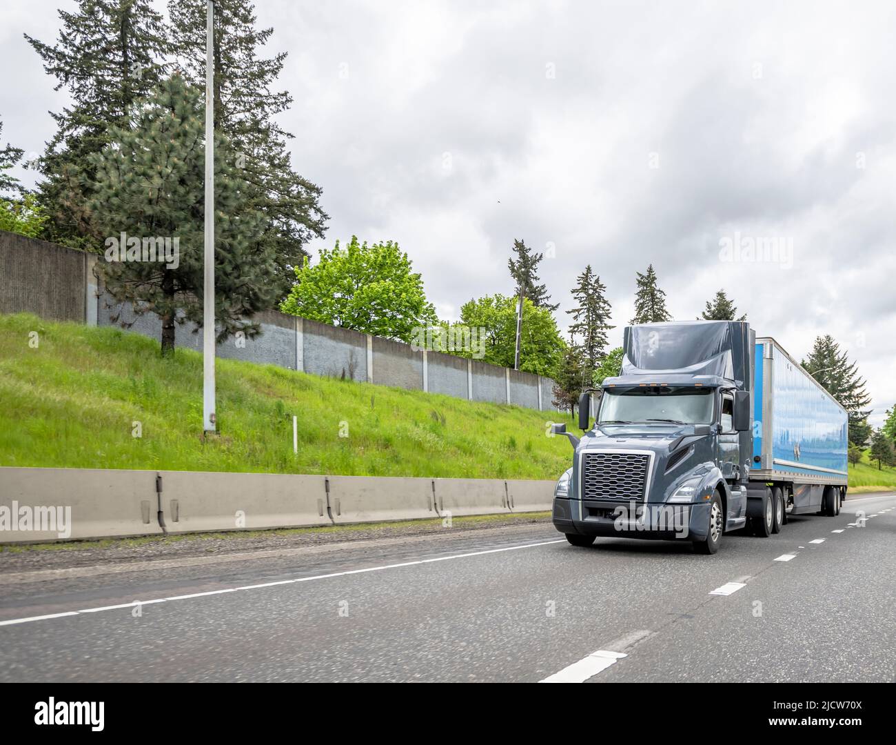 Loaded classic big rig industrial gray semi truck tractor transporting commercial cargo in dry van semi trailer running on the wide straight highway r Stock Photo