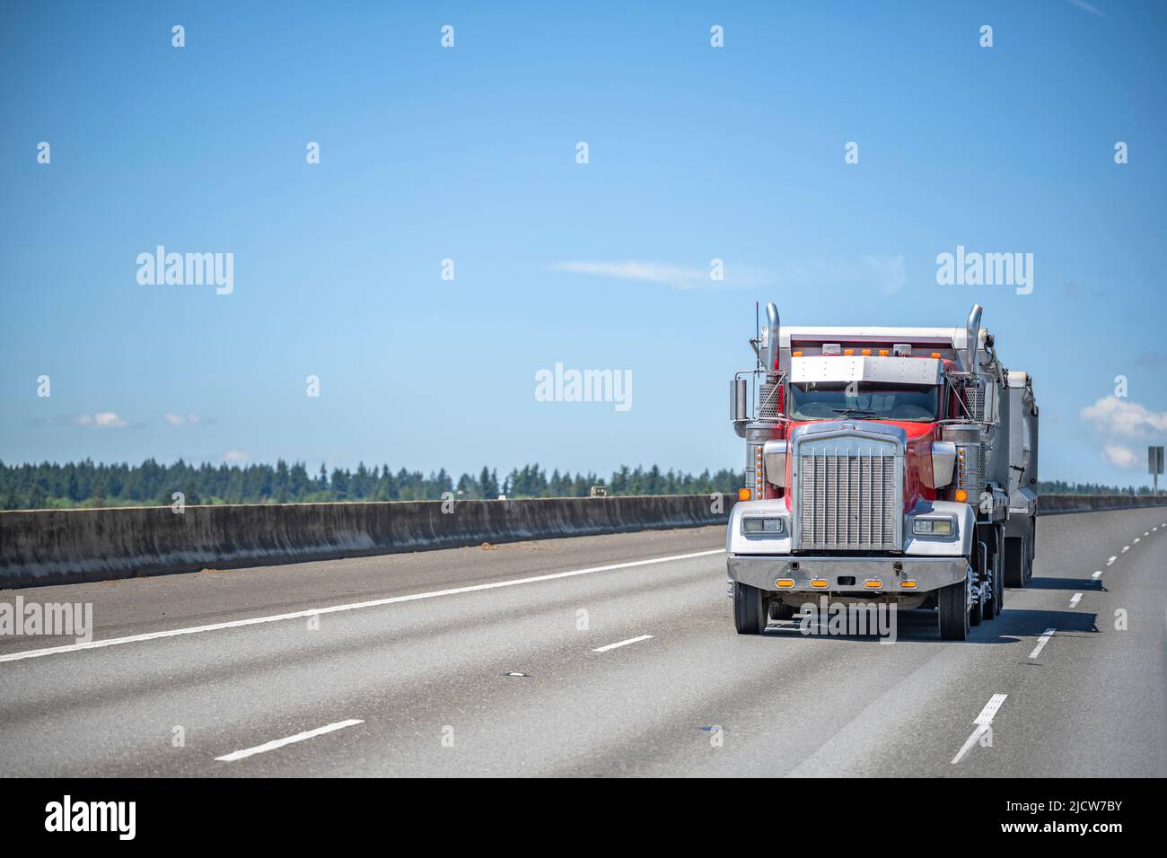 Powerful red big rig bonnet industrial tipper truck tractor transporting commercial cargo in two tip trailers driving for delivery on the wide multili Stock Photo