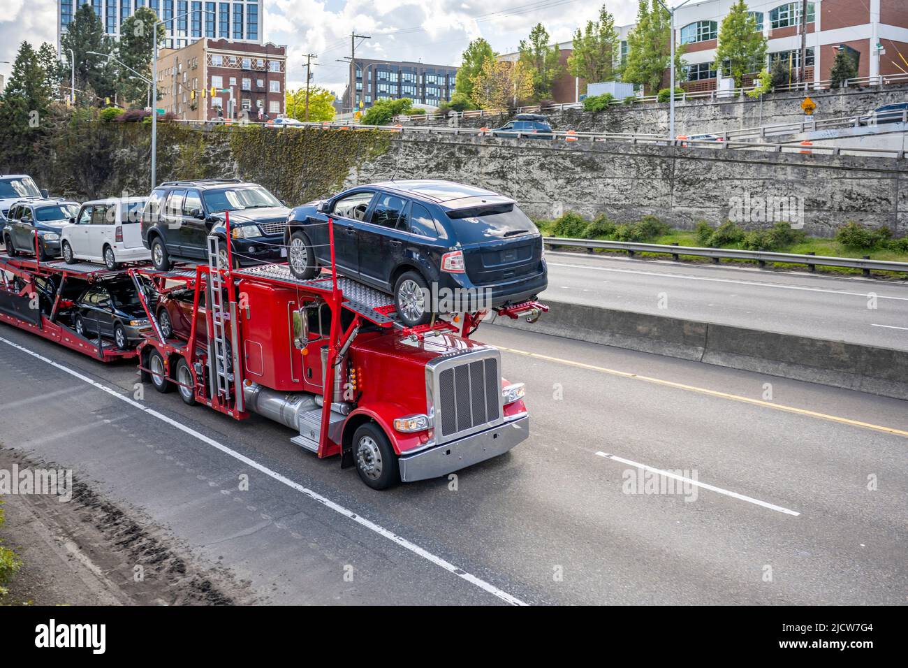 Loaded big rig industrial red car hauler semi truck tractor transporting vehicles on the modular hydraulic semi trailer running on the highway road at Stock Photo