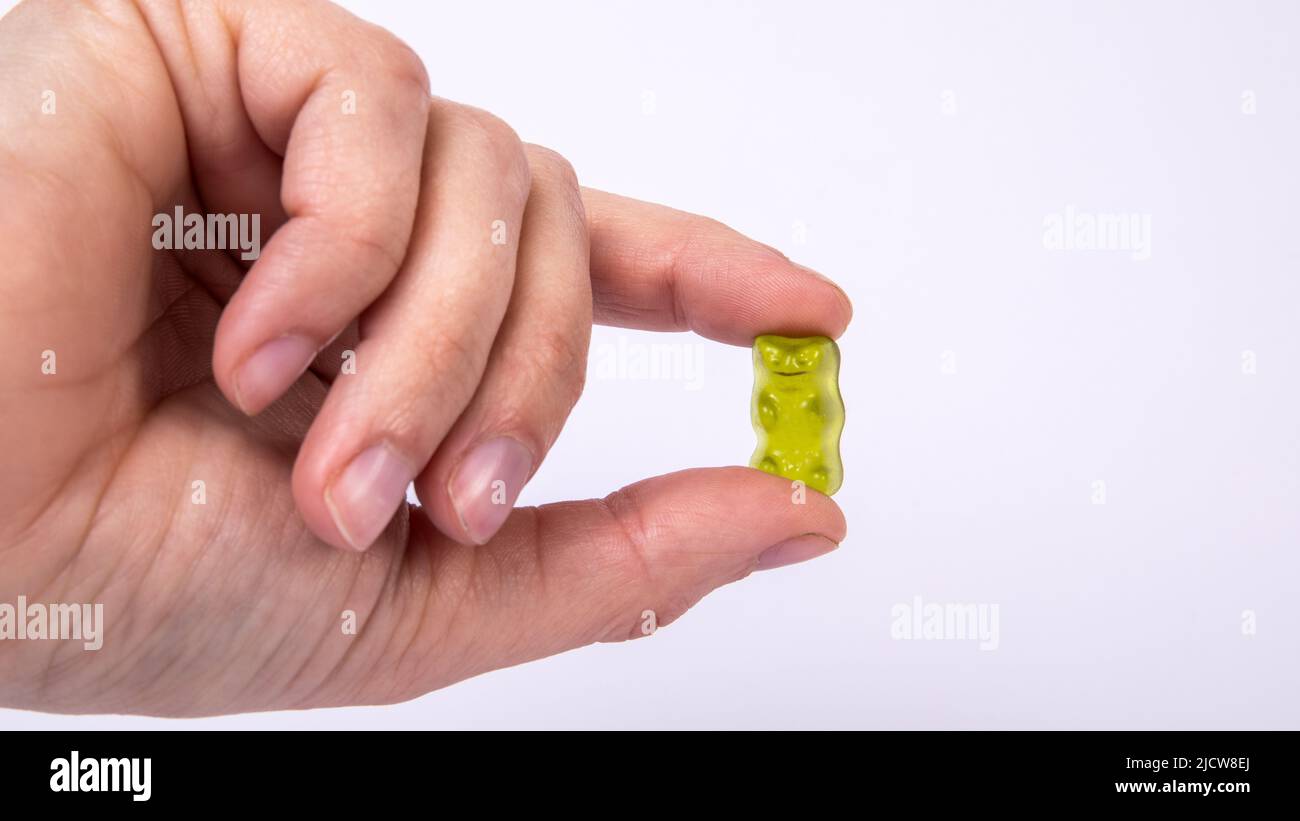 Green rubber candy bear in hand of woman on a white background. Stock Photo