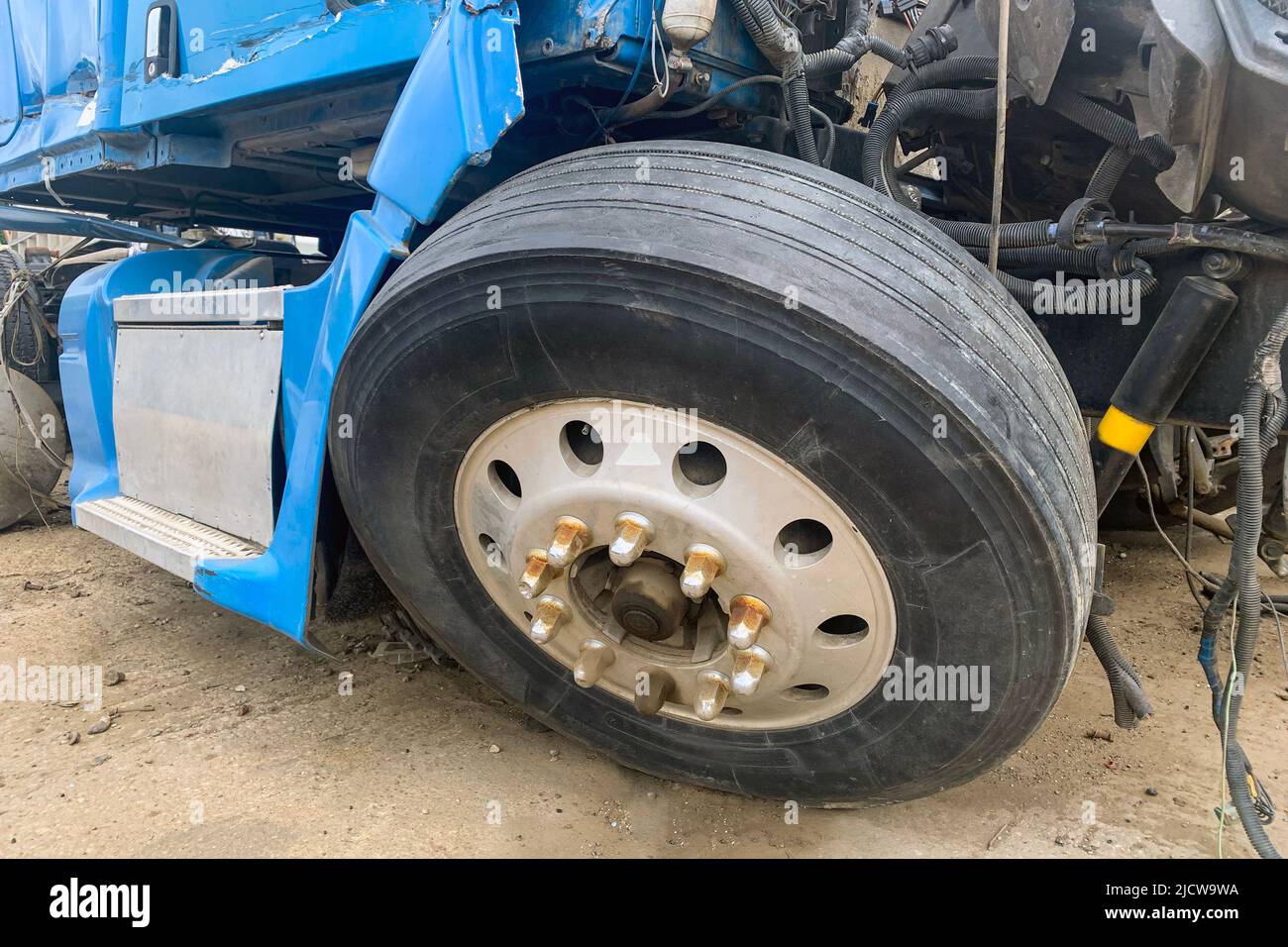 Closeup of abandoned truck in a junkyard, a blue lorry with a destroyed wheel and other parts after an accident on the road, big broken automobile on a junk yard. Stock Photo