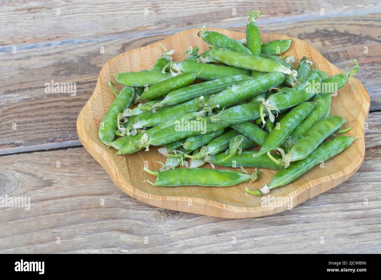 Closeup shot of fresh green peas with seed pods in the plate with wooden background Stock Photo