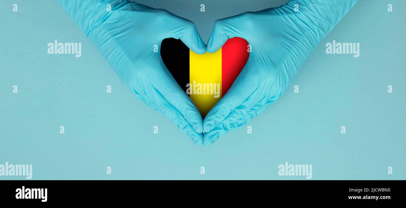 Doctors hands wearing blue surgical gloves making hear shape symbol with Belgium flag Stock Photo