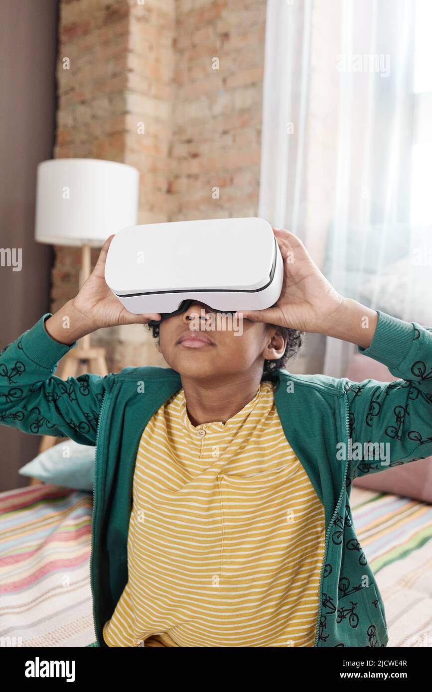 African little boy sitting on sofa in virtual reality headset and watching movie in 3d Stock Photo