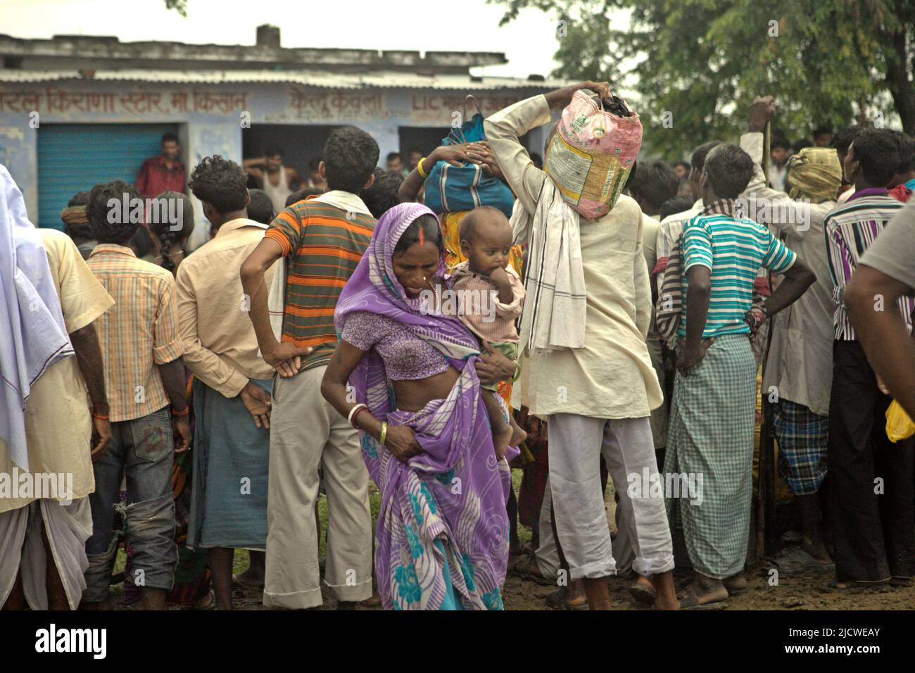 A woman carrying a baby as she is standing in the back of a crowd of people watching an acrobatic, gymnastic stunt performance on the side of the a road on the outskirts of Rajgir in Bihar, India. The India government's Sample Registration System (SRS) reported that the country's Infant Mortality Rate (IMR) was 20 in 2020, meaning that out of 1,000 babies born in the country, 20 die within 12 months of their births, according to the country's statistics quoted by Neeta Lal, a Delhi-based editor and journalist in a feature reporting published by The Diplomat on June 15, 2022. Stock Photo