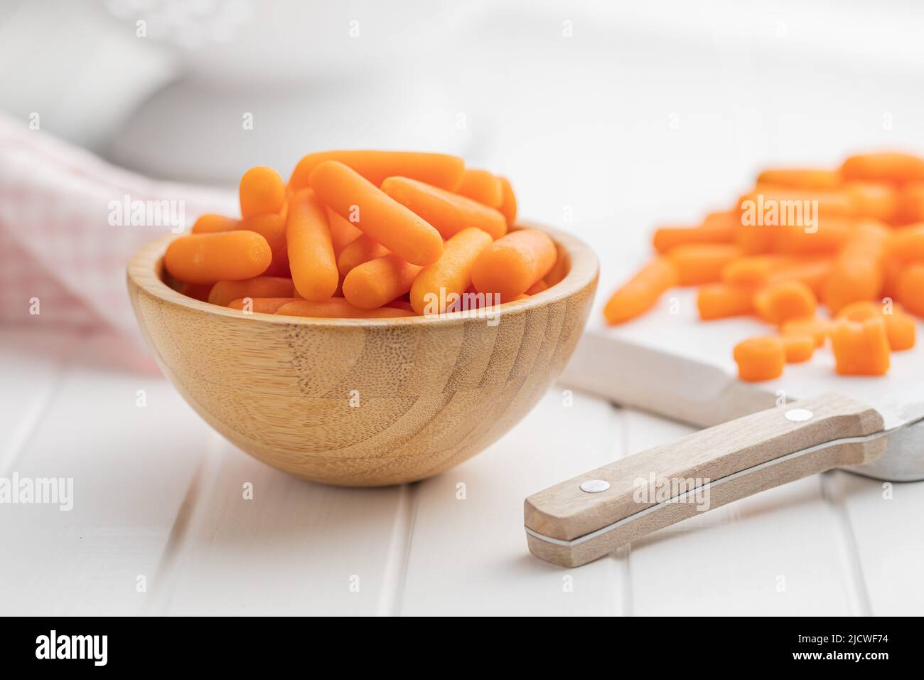 Baby carrot vegetable in bowl. Mini orange carrots on white table. Stock Photo