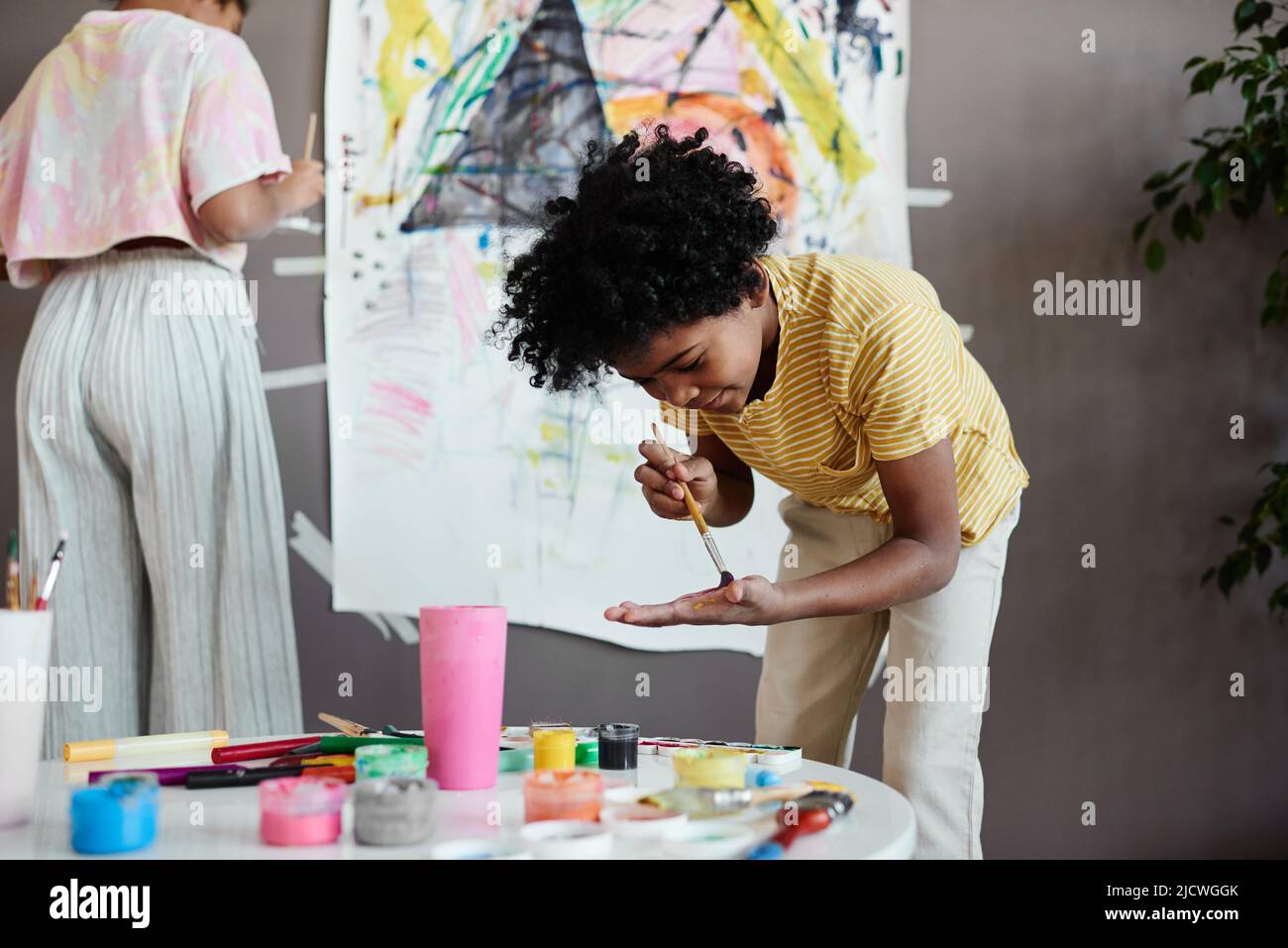 African little boy mixing colors on his hand with paintbrush while painting a big picture together with his sister Stock Photo