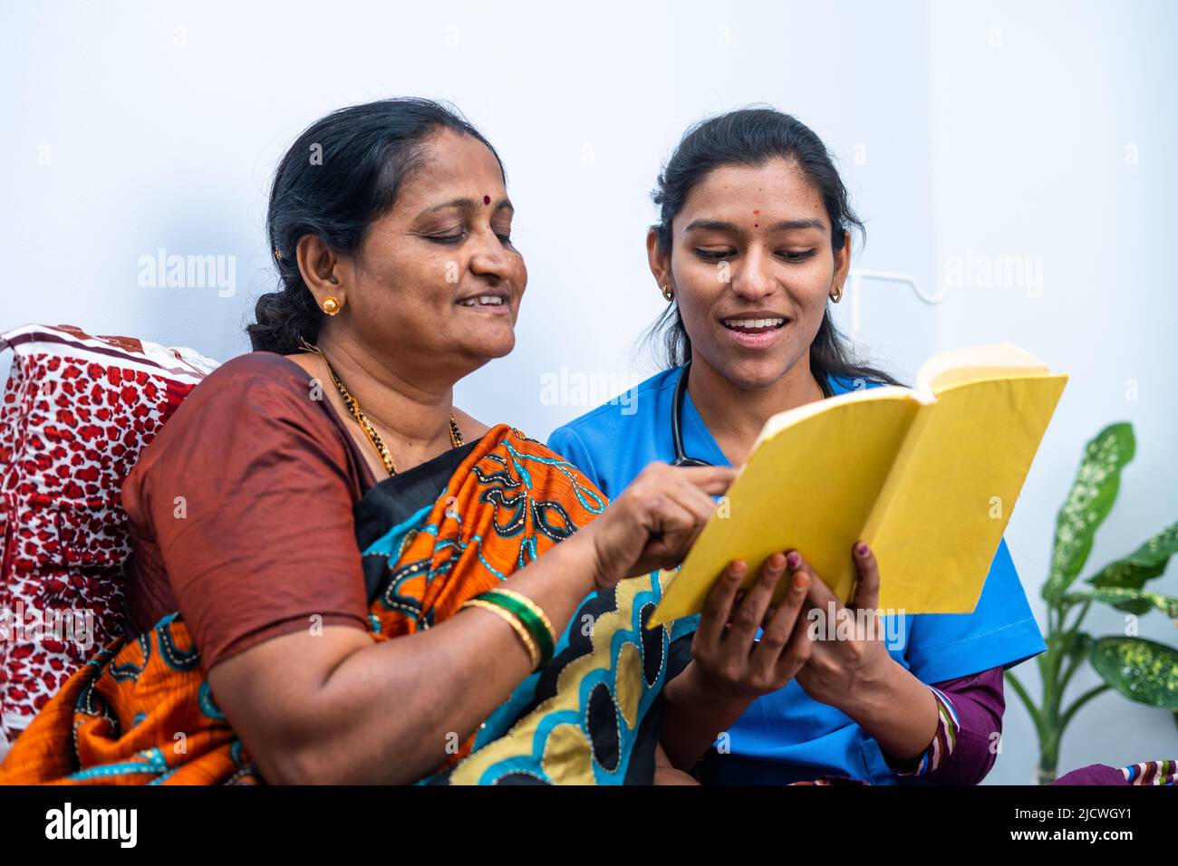 Nurse and sick women laughing by reading story from book at home - concept of relaxation, happiness and caring. Stock Photo