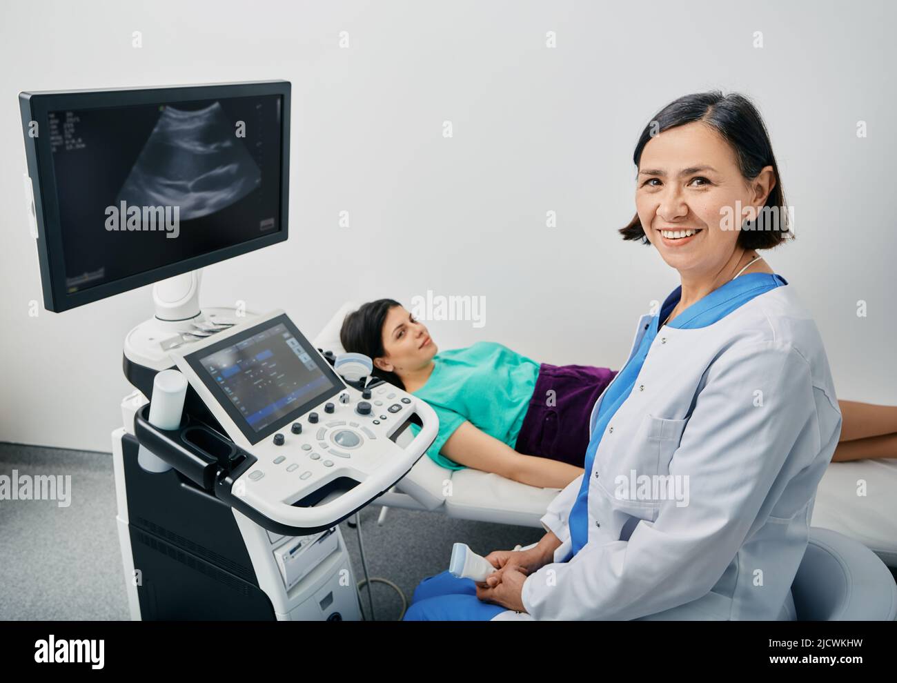 Portrait of sonographer near the ultrasound machine at medical clinic during female patient's body ultrasound scan. Sonographer occupation Stock Photo