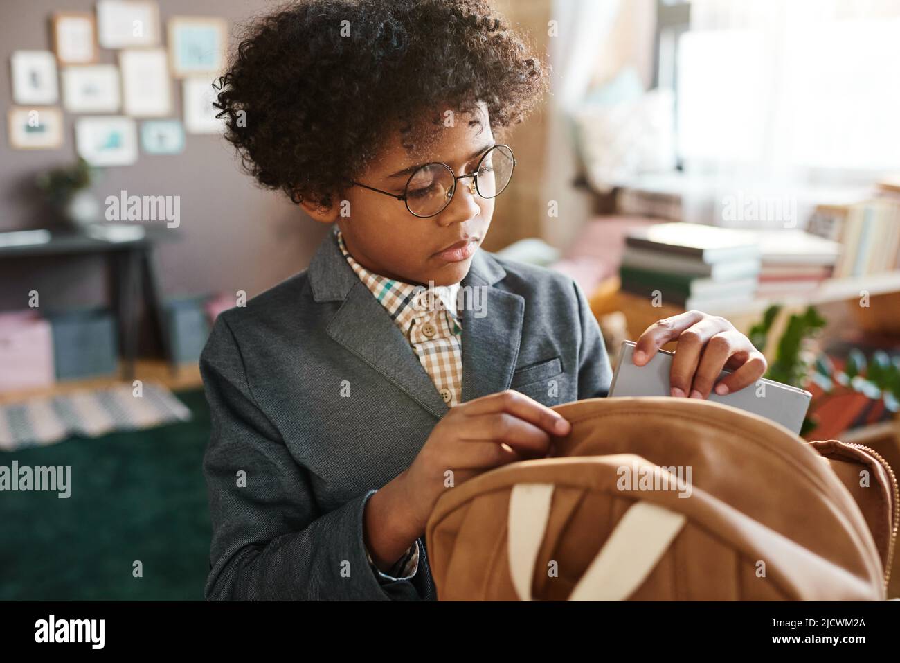 African school boy in eyeglasses and formal suit packing books in his school bag, he preparing for school at home Stock Photo