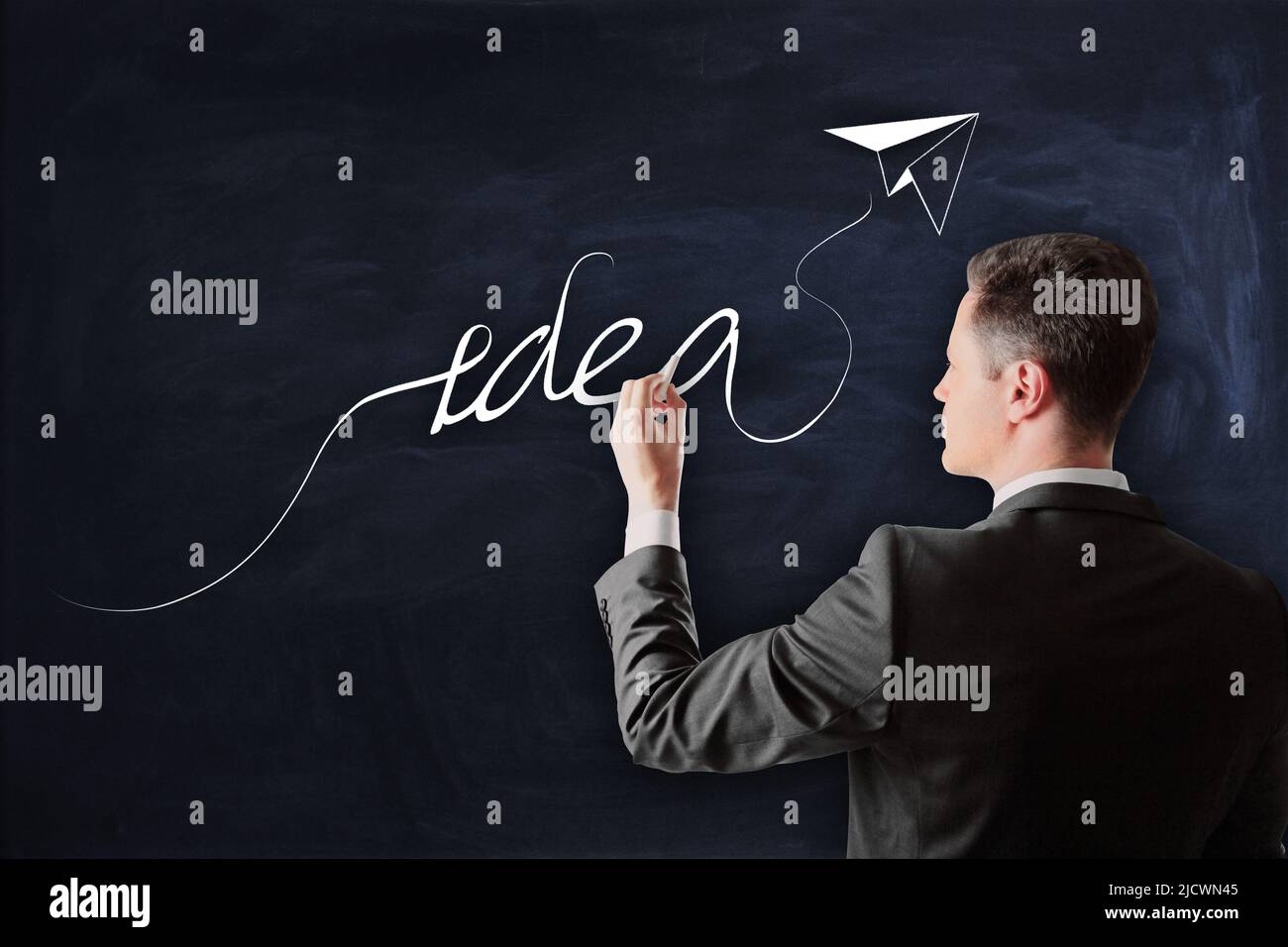 Idea, creativity and strategy concept with man in black suit writing by chalk idea word with paper plane on blackboard Stock Photo