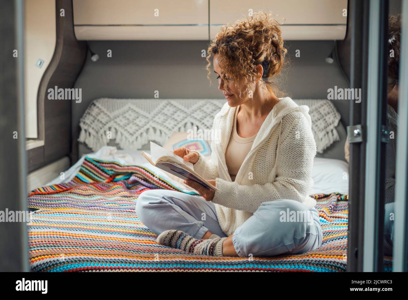 Woman relax sitting on the bed inside comfortable camper van reading a