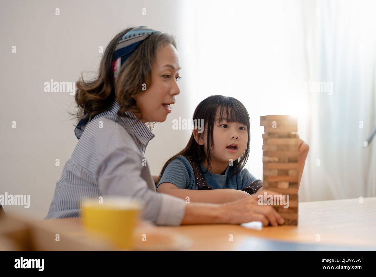 Happy moments of Asian grandmother with her granddaughter playing jenga constructor. Leisure activities for children at home Stock Photo