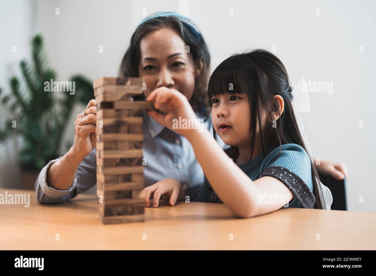 Happy moments of Asian grandmother with her granddaughter playing jenga constructor. Leisure activities for children at home. Stock Photo