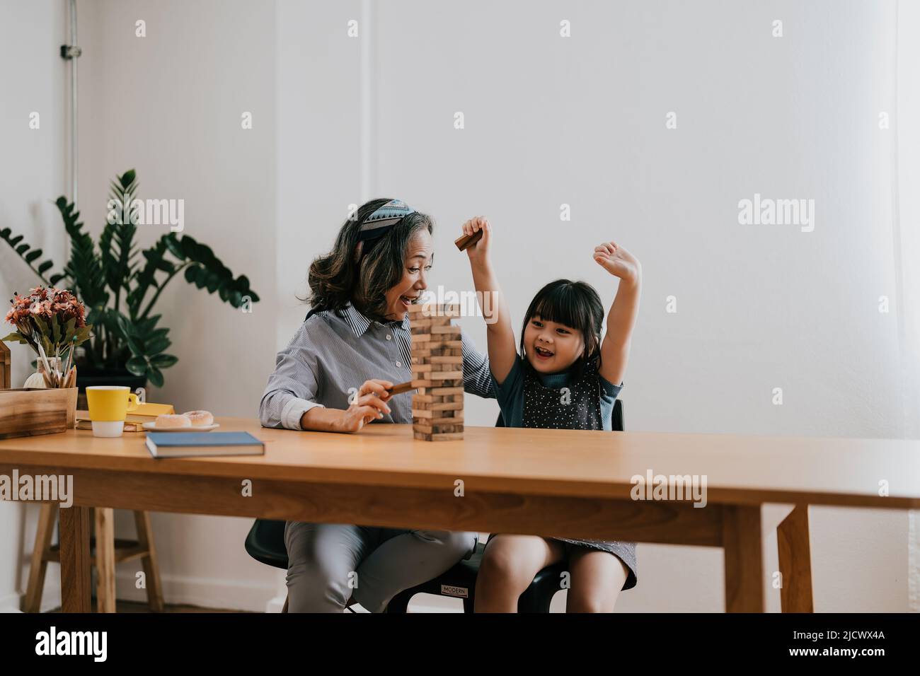 Happy exciting moments of Asian grandmother with her granddaughter playing jenga constructor. Leisure activities for children at home. Stock Photo