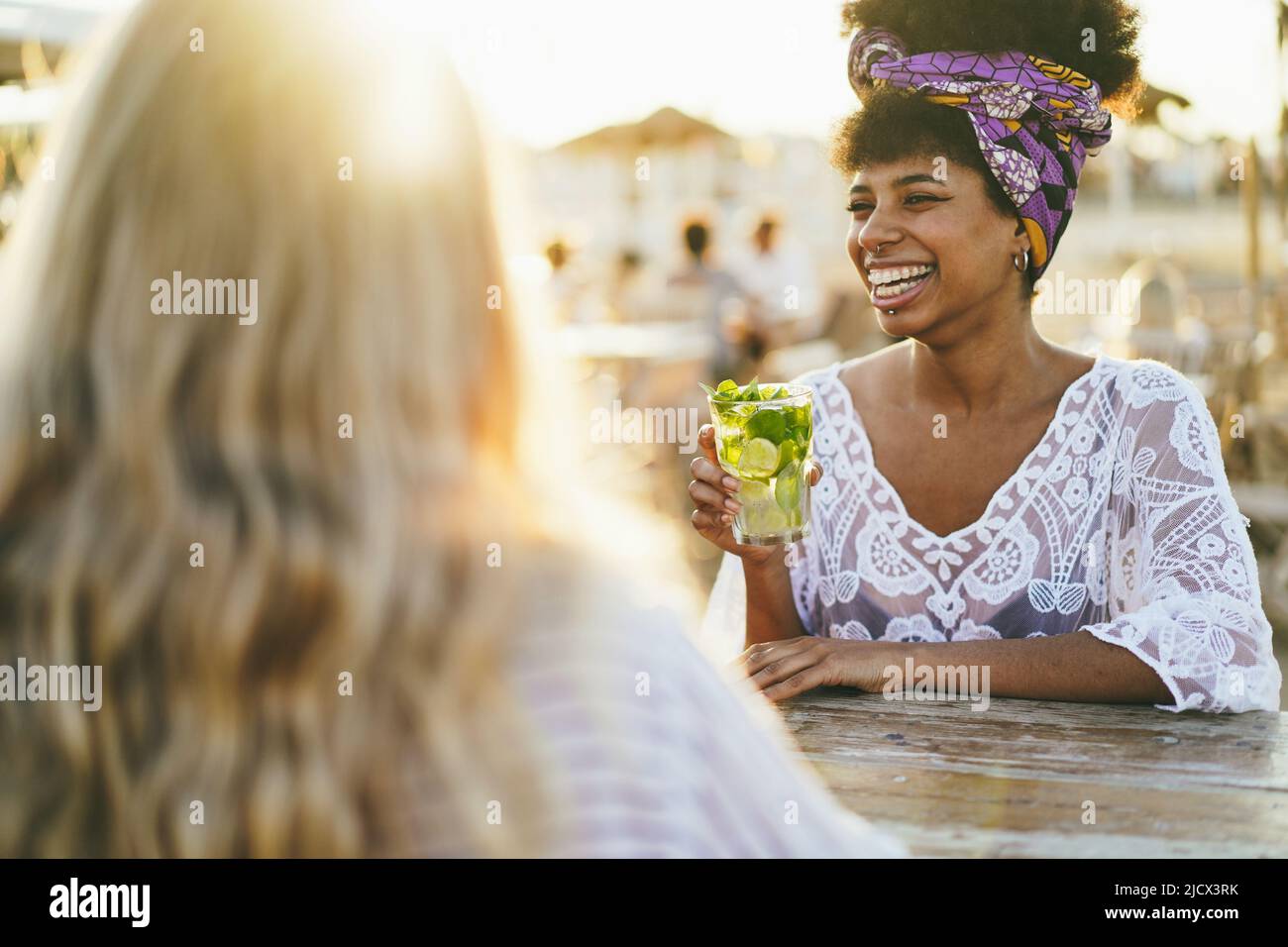 Happy girls having fun drinking alcohol free mojito at cocktail bar on the beach - Summer and vacation concept - Focus on african woman hand holding g Stock Photo