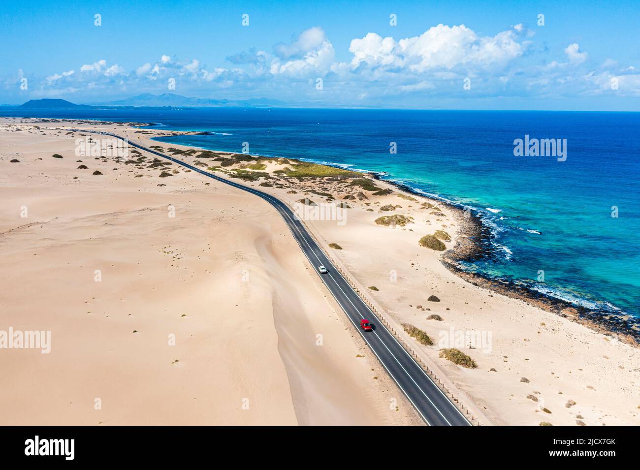 Cars traveling on road in between sand dunes and ocean hires stock