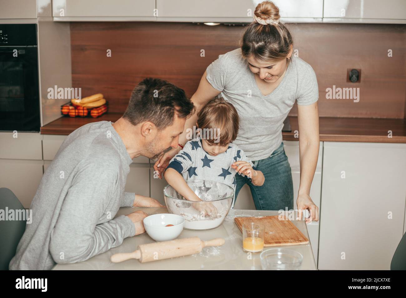 Young cute family of mother, father, son baking cookies in kitchen at home, boy 4 years independently kneads dough, he is keen on process, happy Stock Photo