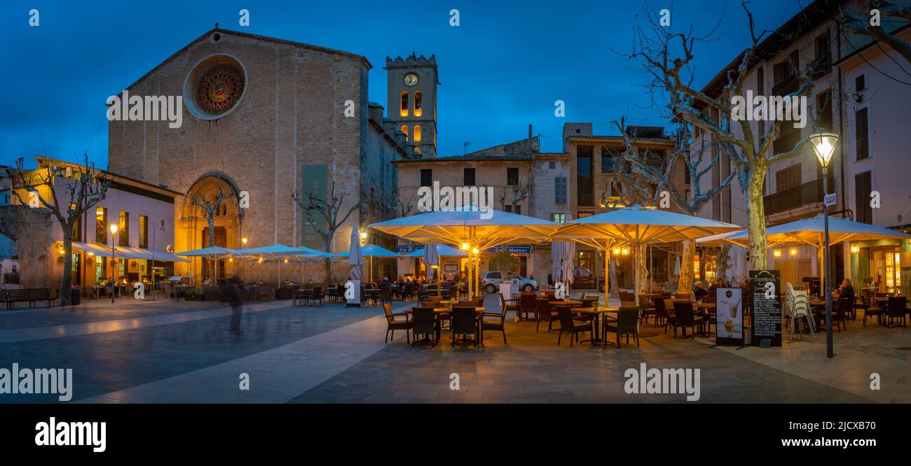 View of Santa Maria Church and people outside bar in Placa Mayor in the old town of Pollenca at dusk, Pollenca, Majorca, Balearic Islands, Spain Stock Photo