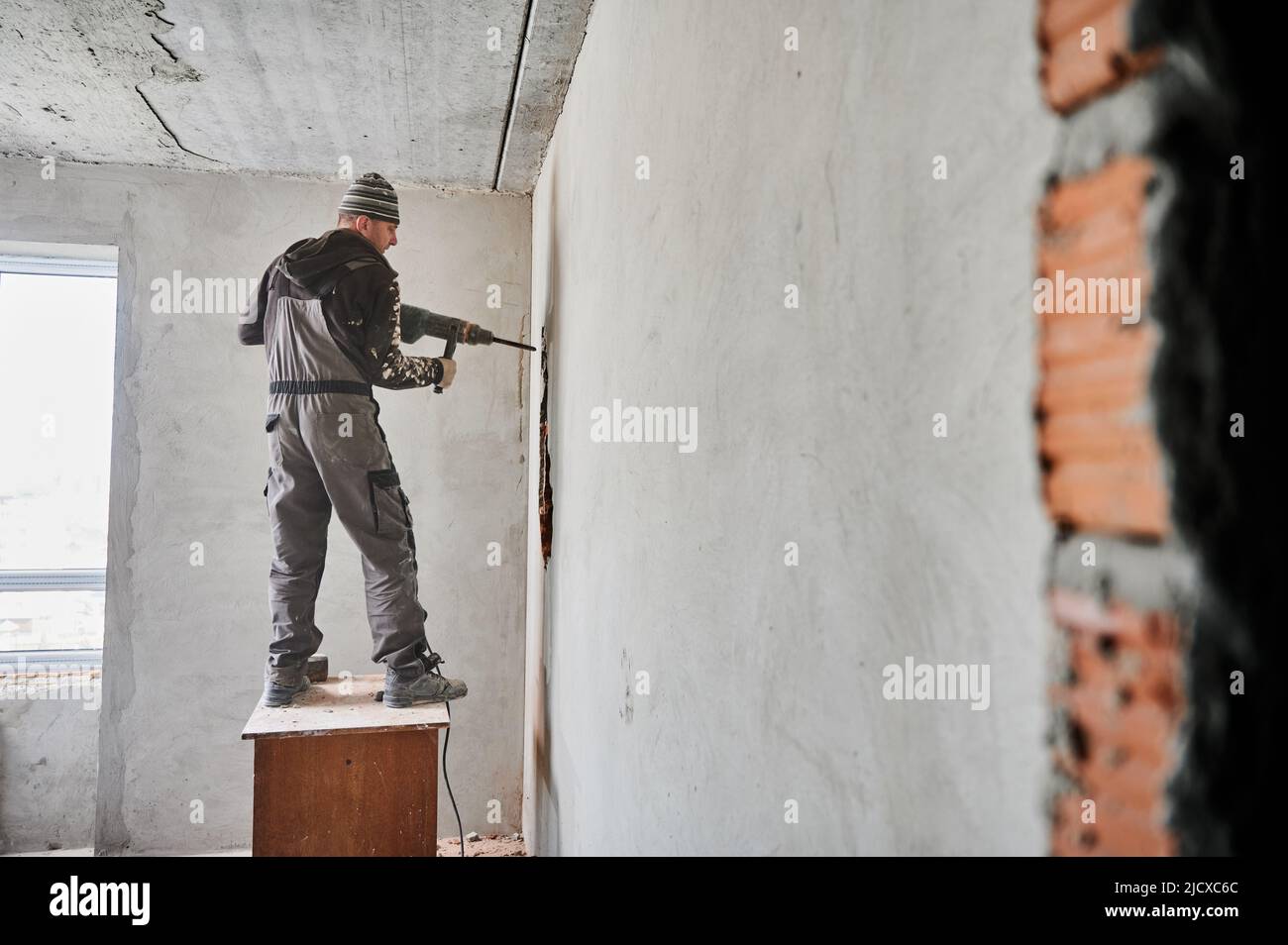 Full length of man builder standing on wooden desk and drilling wall ...