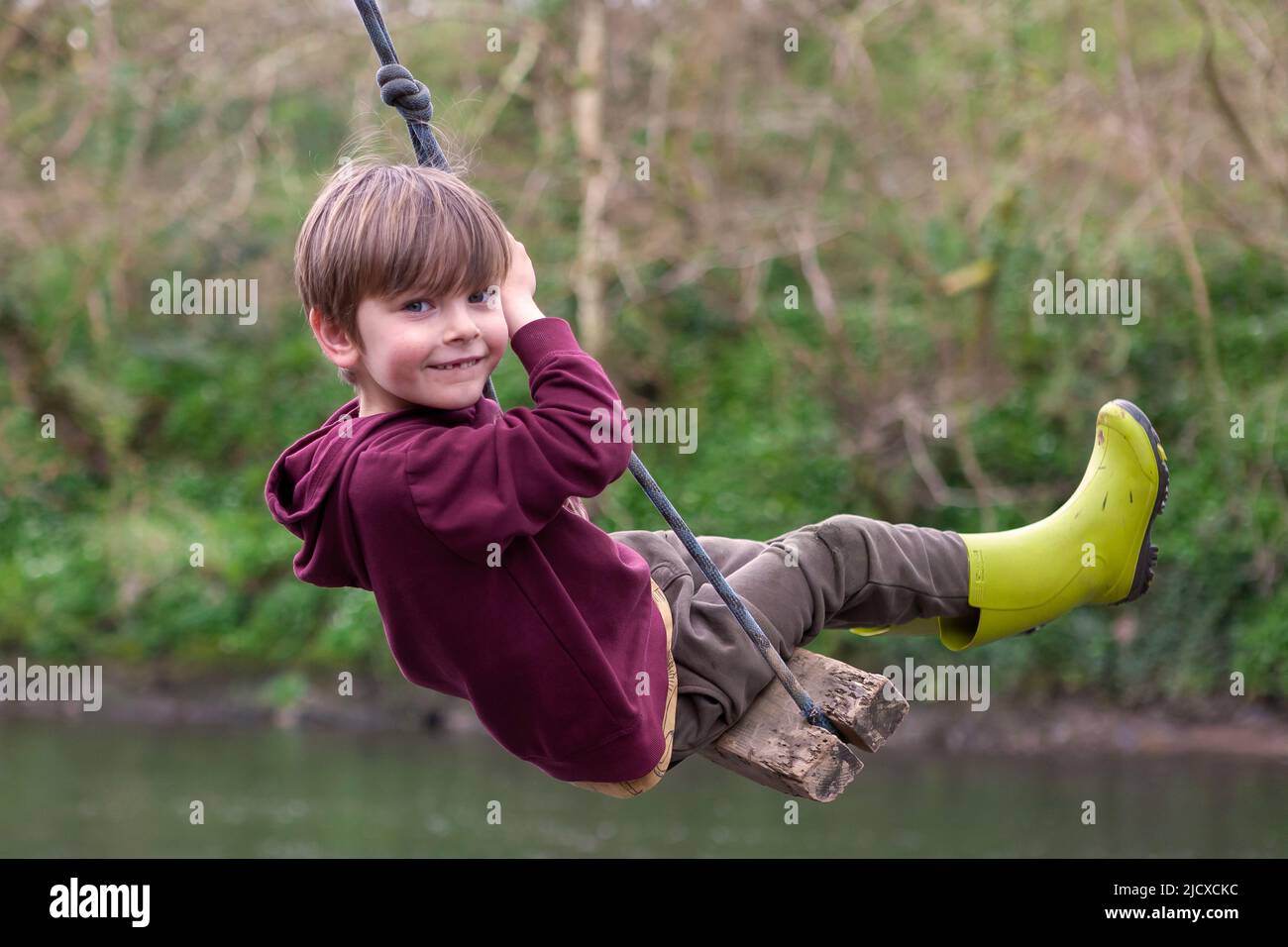 Five-year old boy playing on a rope swing over a river.  MODEL RELEASED Stock Photo