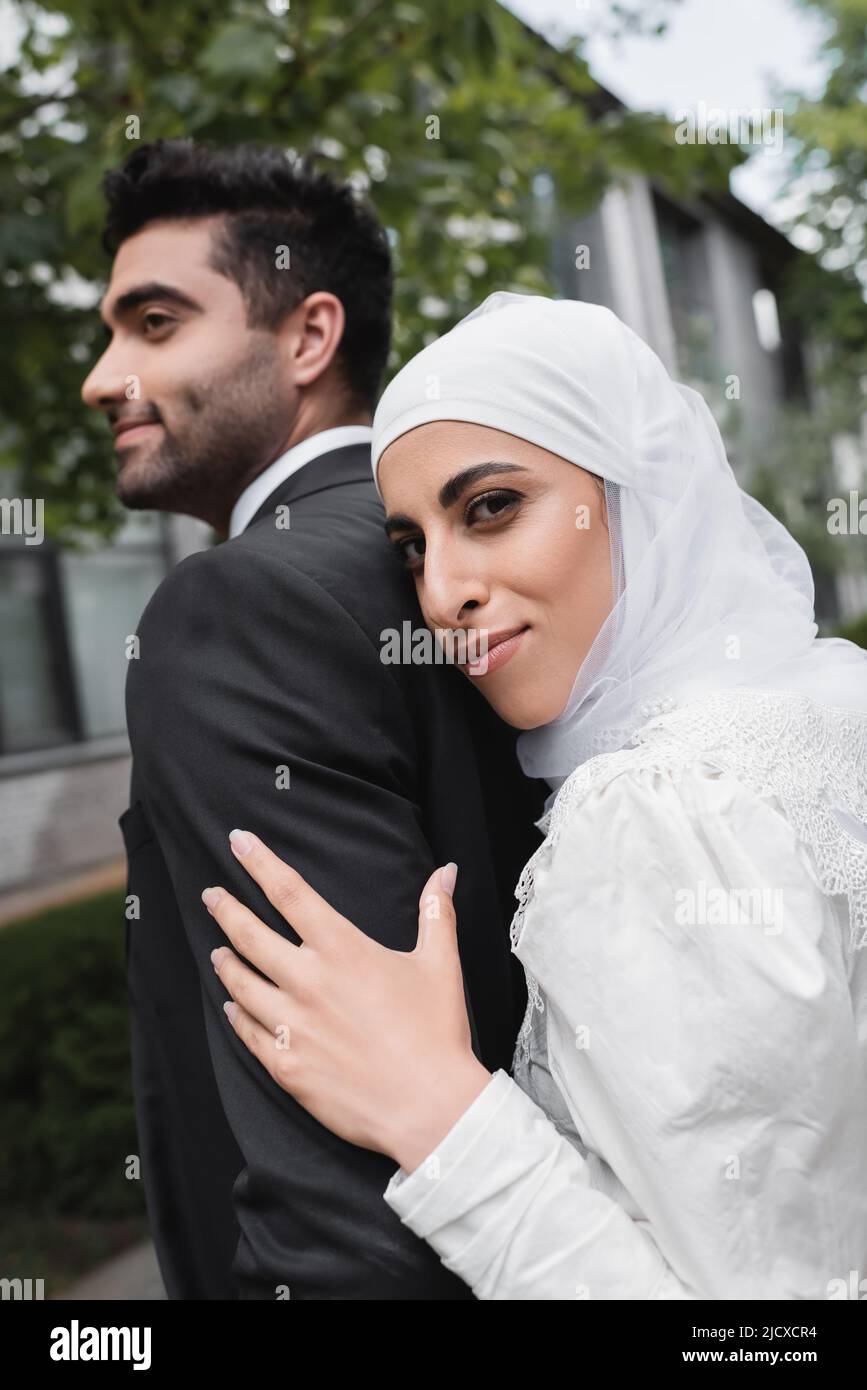 cheerful muslim bride in hijab and wedding dress hugging groom Stock Photo