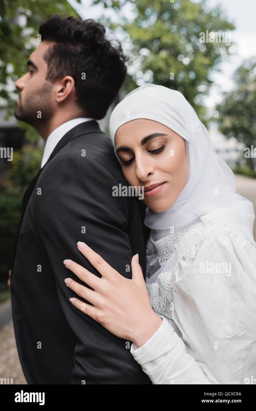 happy muslim bride in hijab and wedding dress hugging groom Stock Photo