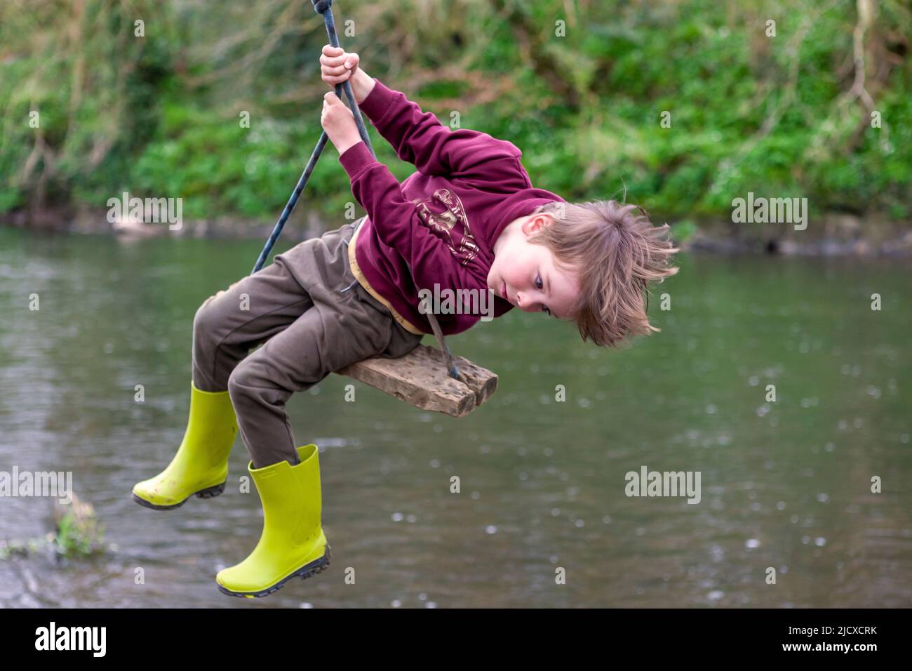 Five-year old boy playing on a rope swing over a river.  MODEL RELEASED Stock Photo