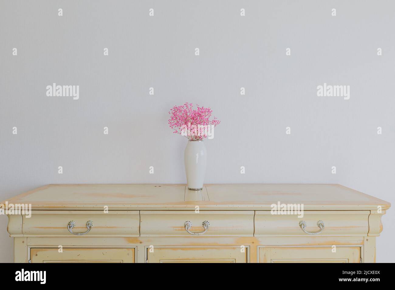 Pink flower in vase standing on dresser Stock Photo