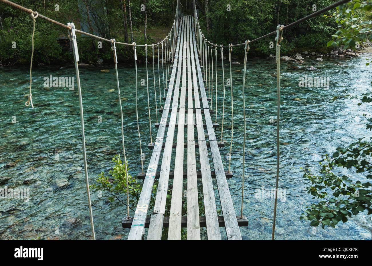 Rickety rope bridge over rushing river Stock Photo