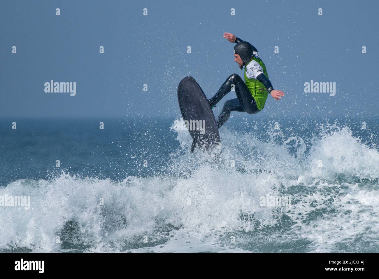 A male surfer wearing a safety helmet competing in a surfing competition at Fistral in Newquay in Cornwall in the UK. Stock Photo