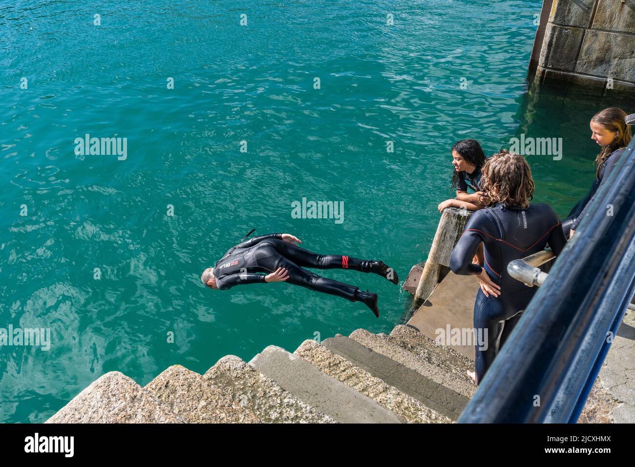 Young teenagers diving into the sea at high tide from the quay in Newquay Harbour in Cornwall in the UK. Stock Photo