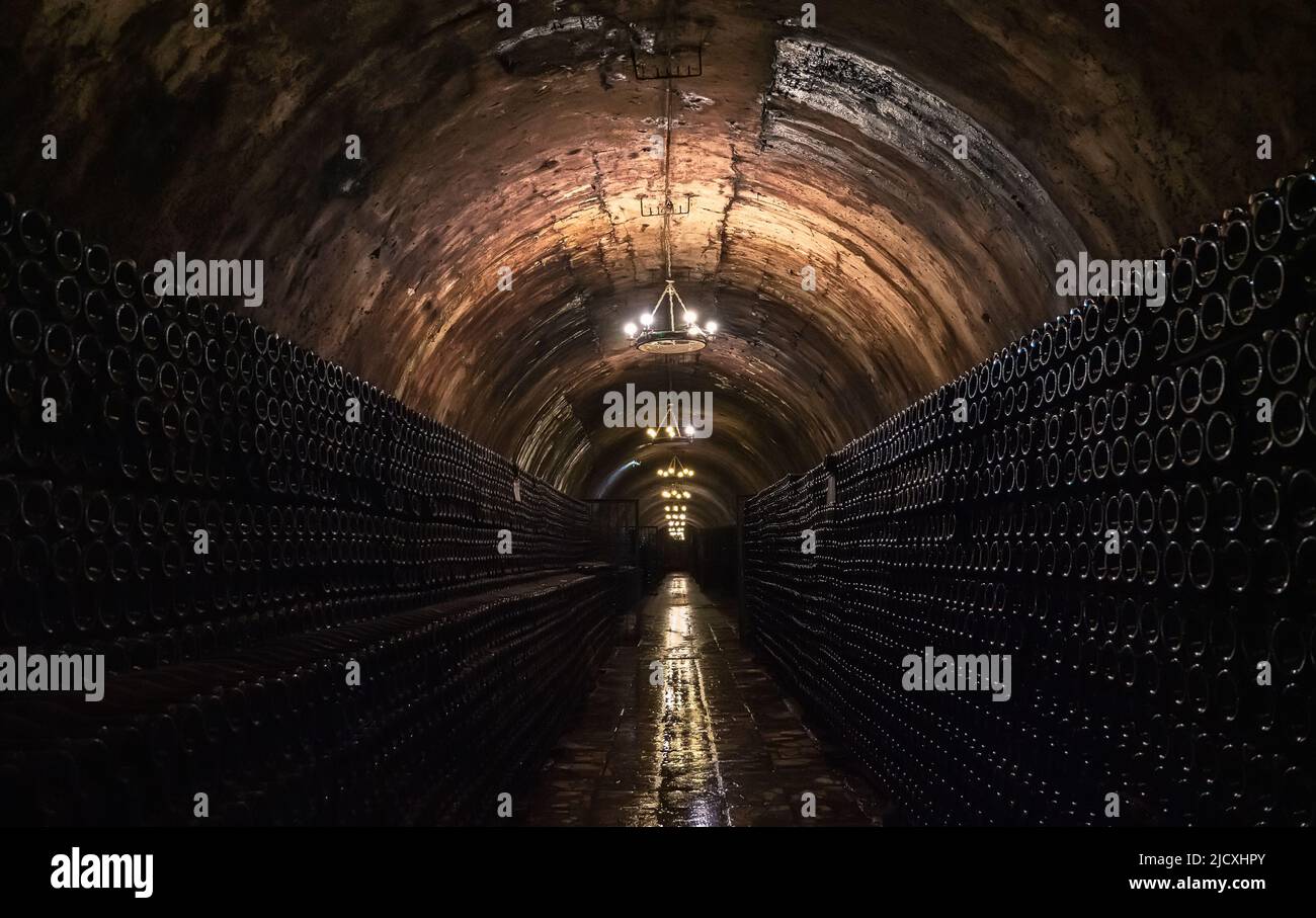 Long underground tunnel in cellar for storage and aging wine in glass bottles. Stock Photo