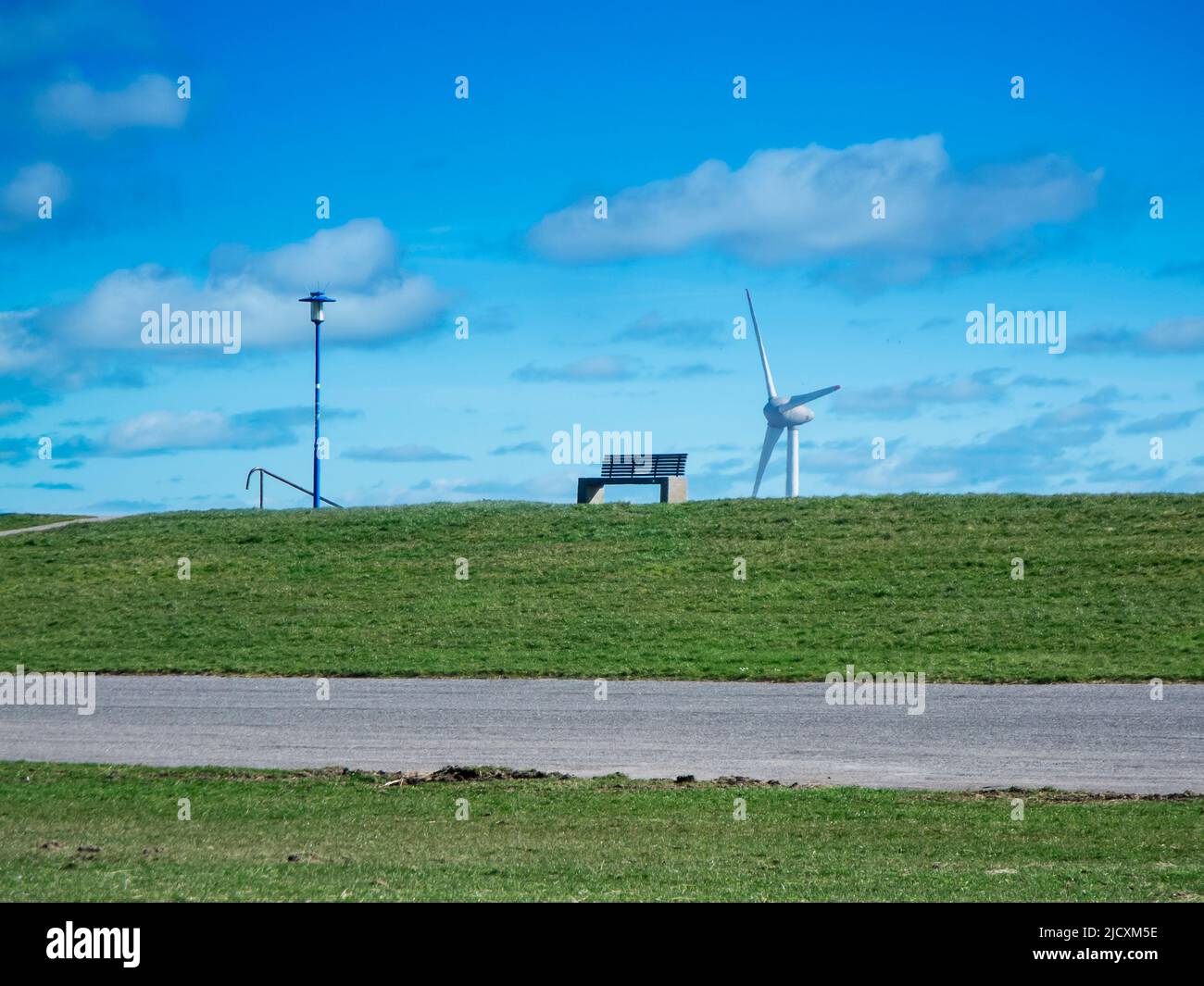 Landscape view of the German North Sea coast with a park bench on the dyke and a street lamp next to it, as well as a wind turbine in the background a Stock Photo