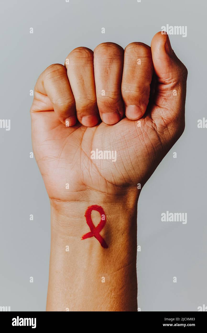 closeup of the raised fist of a man, with a red awareness ribbon painted in his wrist, for the fight against AIDS, on an off-white background Stock Photo